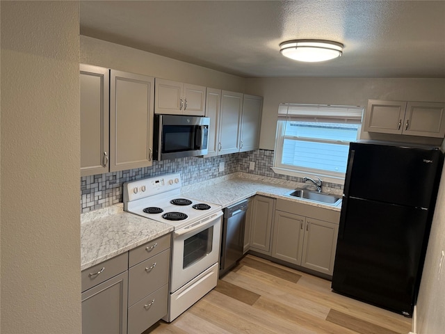 kitchen featuring backsplash, sink, gray cabinets, light wood-type flooring, and stainless steel appliances