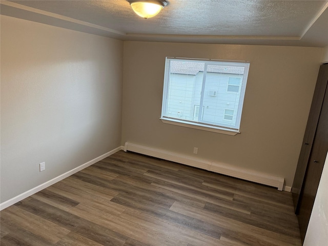 spare room with a raised ceiling, dark hardwood / wood-style flooring, a textured ceiling, and a baseboard heating unit