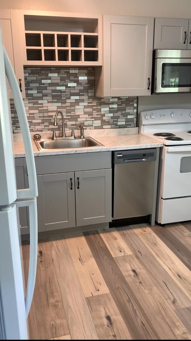 kitchen with light wood-type flooring, backsplash, gray cabinetry, stainless steel appliances, and sink