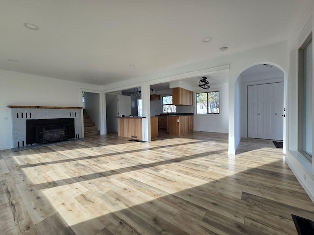 unfurnished living room with sink, light hardwood / wood-style flooring, and a brick fireplace