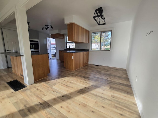 kitchen with sink, black oven, kitchen peninsula, and light hardwood / wood-style flooring