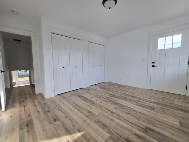 unfurnished bedroom featuring light wood-type flooring and two closets