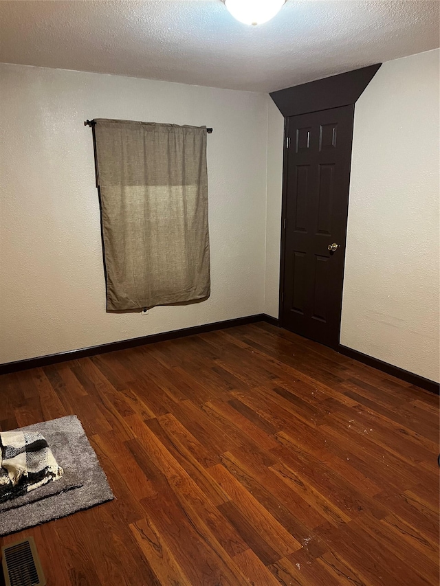 spare room with a textured ceiling and dark hardwood / wood-style floors