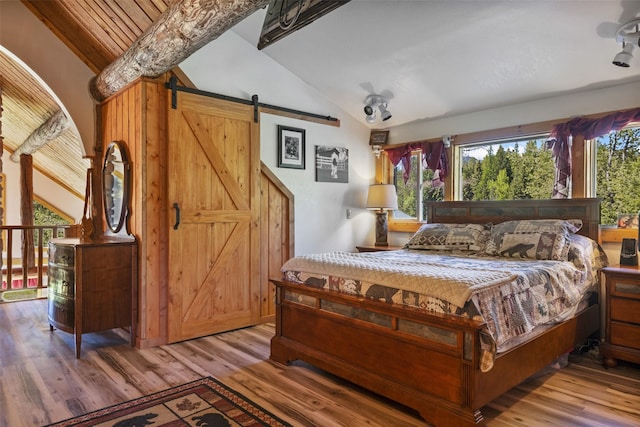 bedroom featuring light hardwood / wood-style floors, ceiling fan, vaulted ceiling, and a barn door