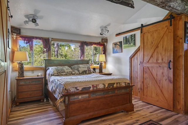 bedroom with hardwood / wood-style flooring, vaulted ceiling, a barn door, and multiple windows