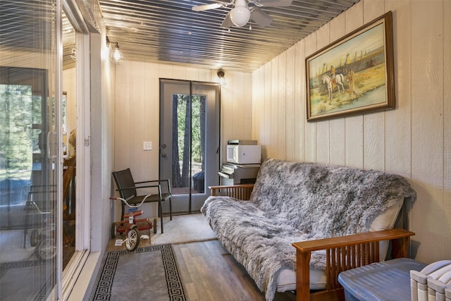 sitting room featuring wood-type flooring, wooden walls, ceiling fan, and wood ceiling