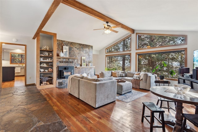 living room with lofted ceiling with beams, a stone fireplace, ceiling fan, and dark wood-type flooring