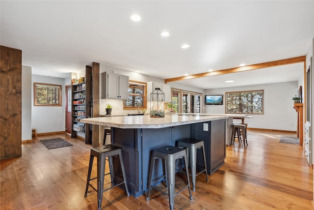 kitchen with a kitchen breakfast bar, light wood-type flooring, gray cabinetry, sink, and a large island