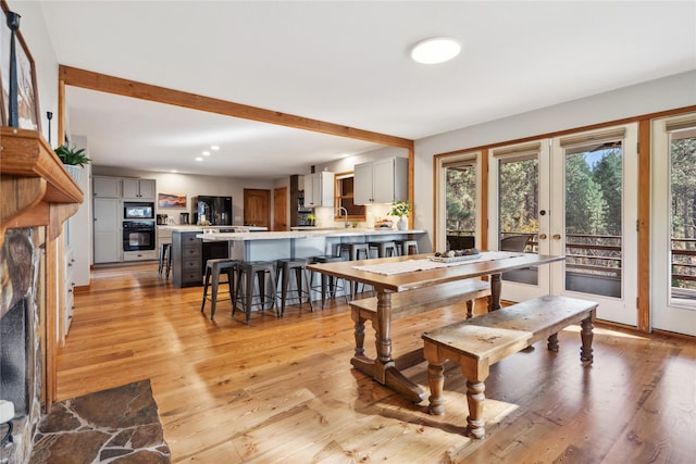 dining area with a fireplace, light wood-type flooring, sink, and french doors