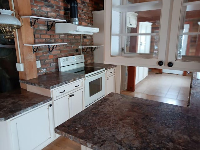 kitchen with white range with electric stovetop, dark stone counters, white cabinets, and extractor fan