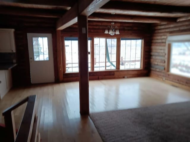 unfurnished living room featuring beam ceiling, log walls, light wood-type flooring, and a notable chandelier