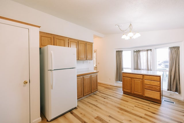 kitchen featuring a notable chandelier, white fridge, pendant lighting, lofted ceiling, and light wood-type flooring