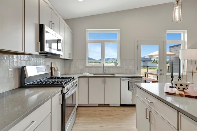 kitchen featuring appliances with stainless steel finishes, lofted ceiling, hanging light fixtures, white cabinets, and sink