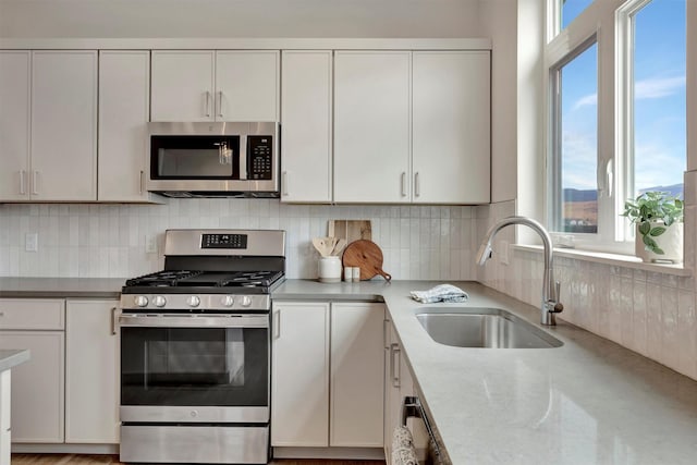 kitchen featuring appliances with stainless steel finishes, white cabinetry, decorative backsplash, sink, and light stone counters