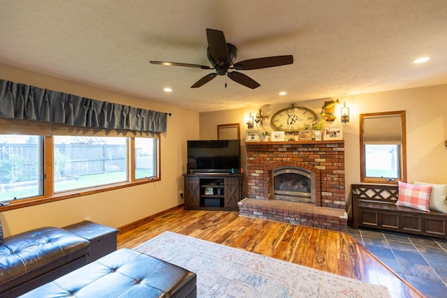 living room featuring ceiling fan, dark wood-type flooring, a brick fireplace, and a textured ceiling