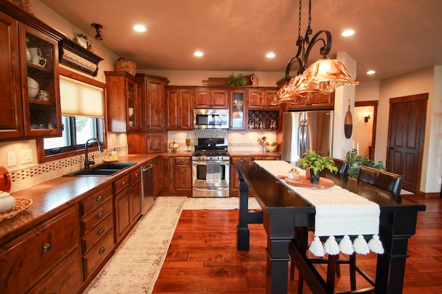 kitchen featuring stainless steel appliances, sink, wood-type flooring, decorative backsplash, and hanging light fixtures