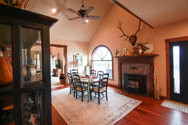 dining space with dark wood-type flooring, high vaulted ceiling, ceiling fan, and a wood stove