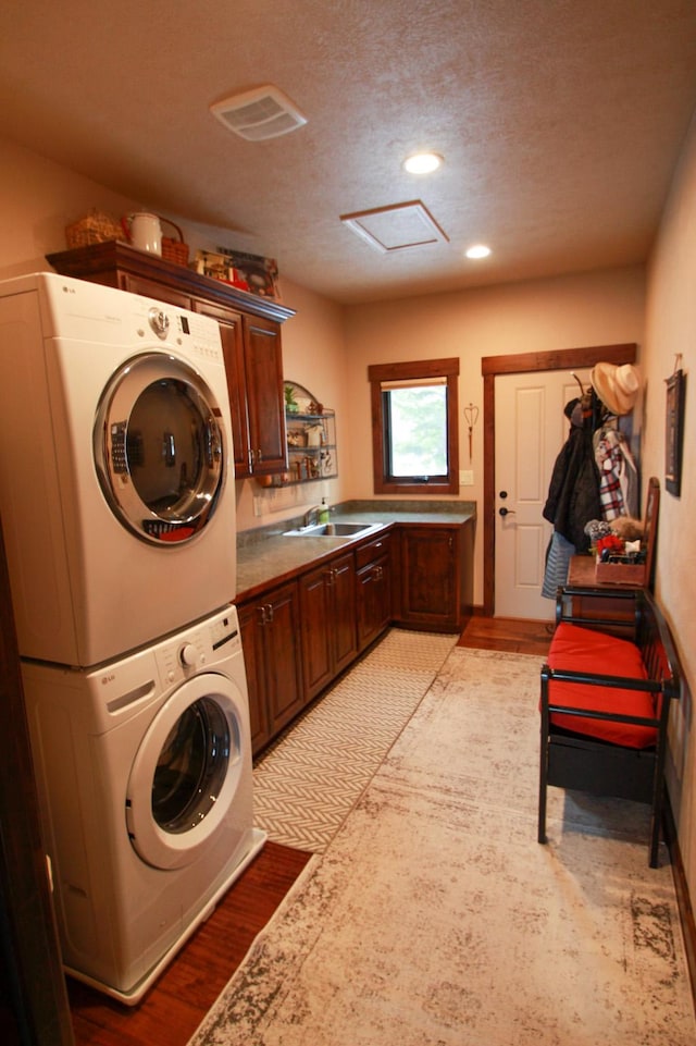 clothes washing area with a textured ceiling, light hardwood / wood-style floors, stacked washer / dryer, and sink