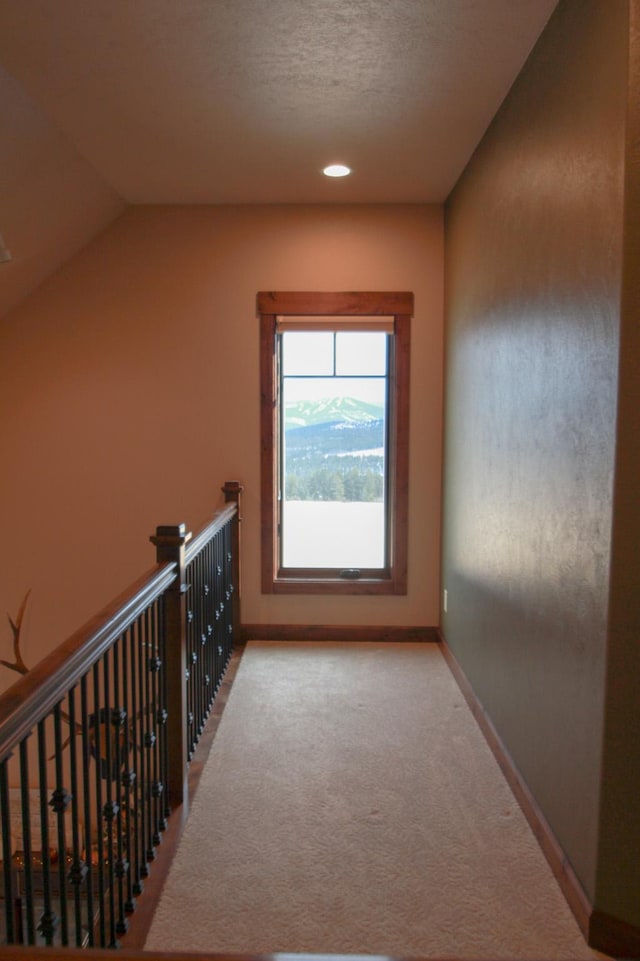 hallway featuring a textured ceiling, light colored carpet, and vaulted ceiling