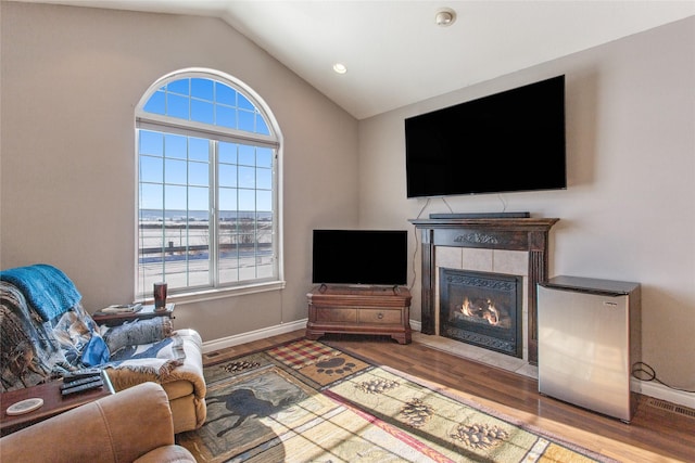 living room with hardwood / wood-style flooring, vaulted ceiling, and a tile fireplace