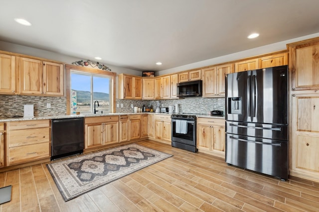 kitchen featuring light stone countertops, black appliances, light wood-type flooring, backsplash, and sink