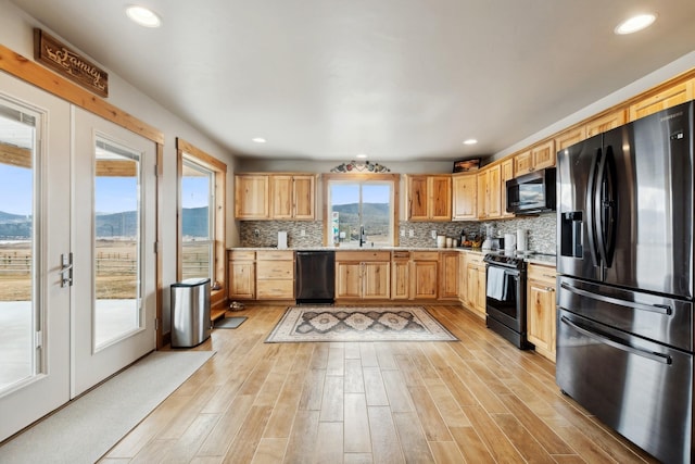 kitchen with sink, light hardwood / wood-style flooring, a mountain view, decorative backsplash, and black appliances