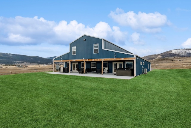 back of property with a yard, a patio area, a hot tub, and a mountain view