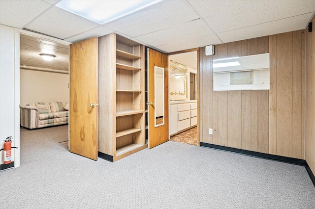 interior space with a paneled ceiling, wood walls, and light colored carpet