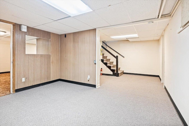 basement with light colored carpet, wood walls, and a paneled ceiling