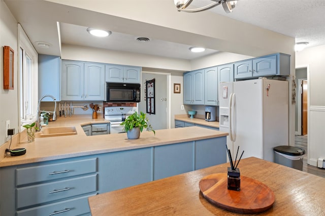 kitchen featuring white appliances, blue cabinetry, kitchen peninsula, a textured ceiling, and sink