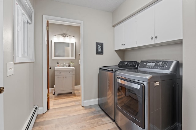 clothes washing area with a baseboard heating unit, light wood-type flooring, cabinets, washer and dryer, and sink