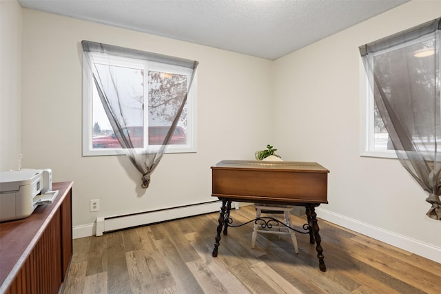 misc room featuring a healthy amount of sunlight, a textured ceiling, hardwood / wood-style flooring, and a baseboard heating unit