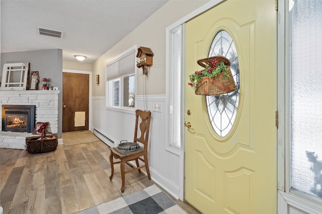 entryway with baseboard heating, a textured ceiling, light hardwood / wood-style floors, and a fireplace