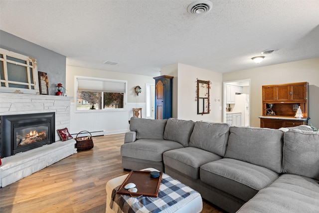 living room with a textured ceiling, a baseboard heating unit, a stone fireplace, and hardwood / wood-style flooring