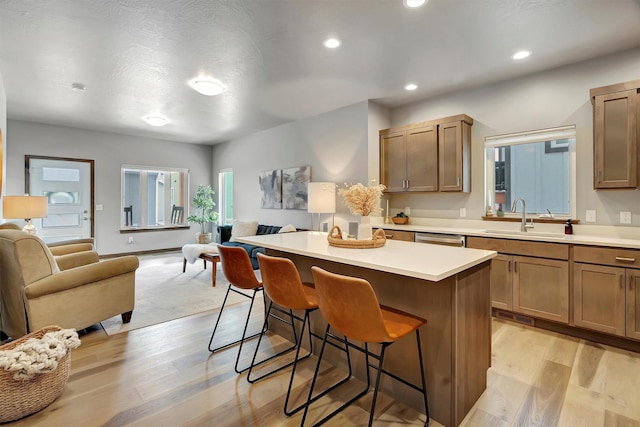 kitchen with light hardwood / wood-style floors, a center island, a kitchen bar, sink, and stainless steel dishwasher