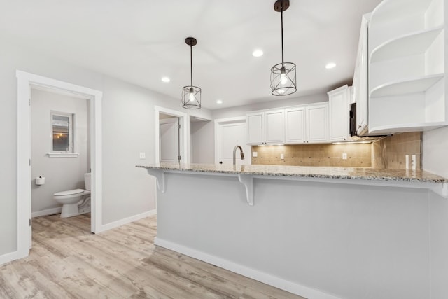 kitchen featuring kitchen peninsula, light stone countertops, hanging light fixtures, decorative backsplash, and white cabinets