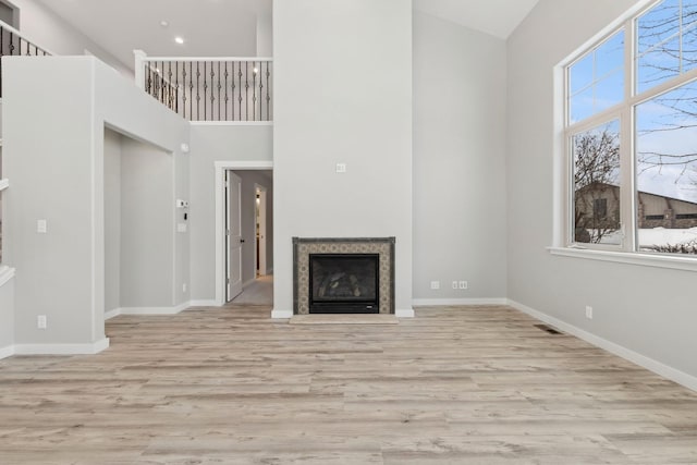 unfurnished living room with a high ceiling, light wood-type flooring, and plenty of natural light