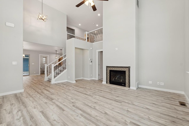 unfurnished living room featuring a towering ceiling, light wood-type flooring, and ceiling fan