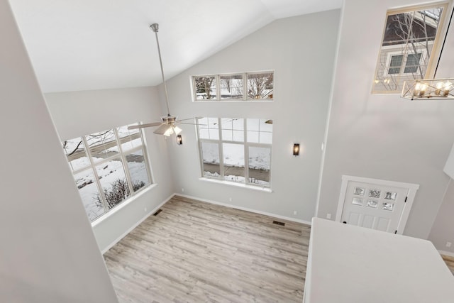 foyer entrance featuring light hardwood / wood-style floors, ceiling fan with notable chandelier, high vaulted ceiling, and plenty of natural light