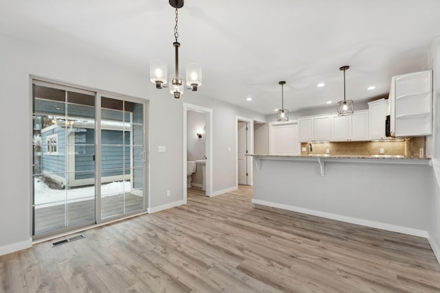 kitchen with white cabinets, a kitchen breakfast bar, light hardwood / wood-style flooring, kitchen peninsula, and pendant lighting