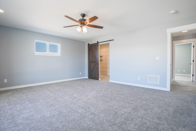 spare room with ceiling fan, a barn door, and carpet flooring