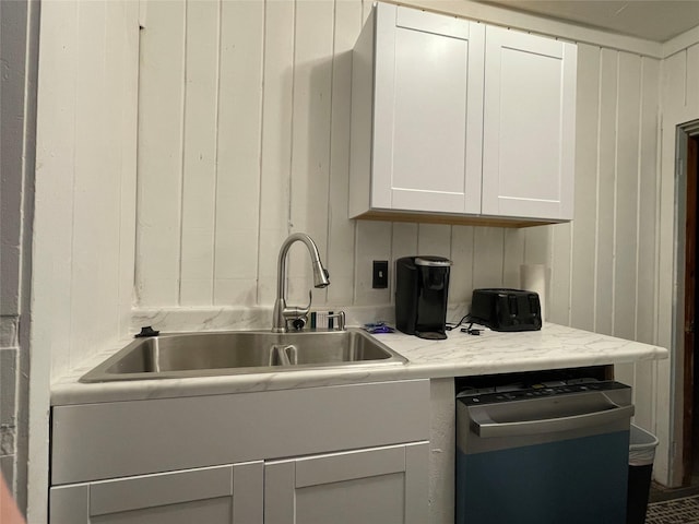 kitchen with white cabinets, wood walls, dishwasher, and sink