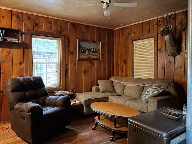 living room with ceiling fan, crown molding, wood walls, and wood-type flooring