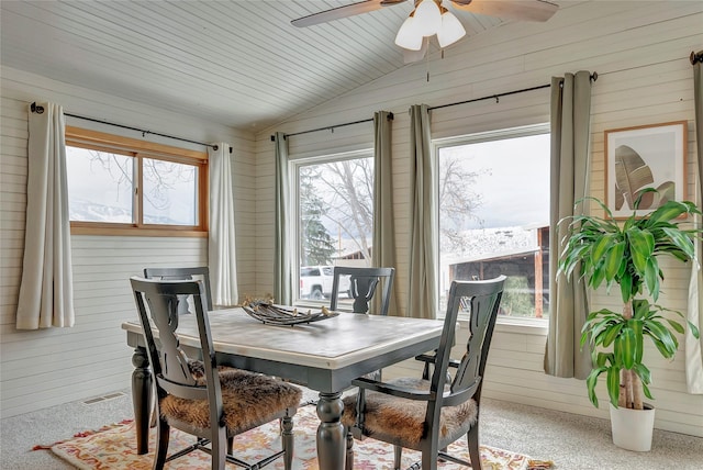 carpeted dining area with ceiling fan, vaulted ceiling, and wooden walls