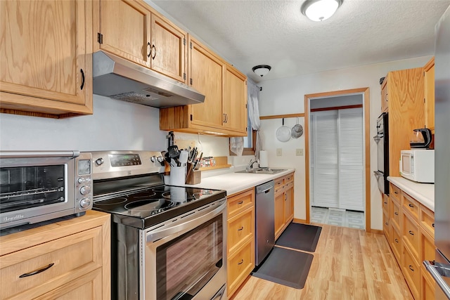 kitchen featuring a textured ceiling, stainless steel appliances, light brown cabinetry, light hardwood / wood-style floors, and sink