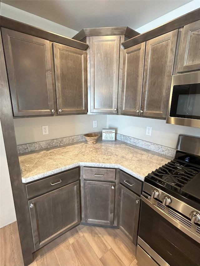 kitchen with light stone countertops, appliances with stainless steel finishes, light hardwood / wood-style floors, and dark brown cabinetry