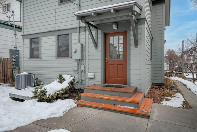 snow covered property entrance with central AC unit