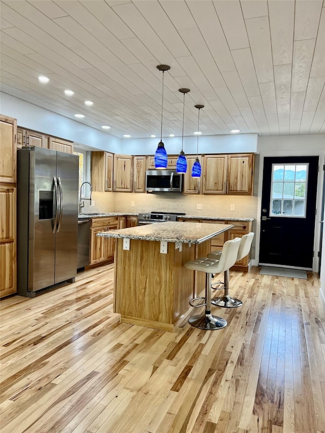 kitchen with stainless steel appliances, wooden ceiling, a center island, light stone counters, and pendant lighting