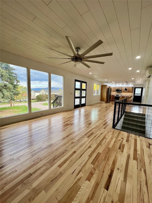 unfurnished living room featuring light wood-type flooring, a wall unit AC, ceiling fan, and wooden ceiling