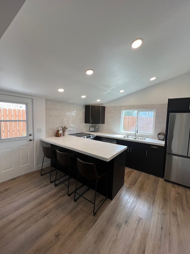 kitchen with sink, vaulted ceiling, a kitchen breakfast bar, kitchen peninsula, and stainless steel refrigerator